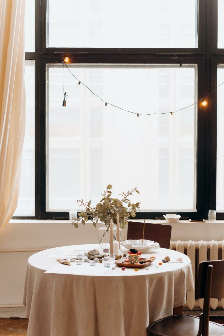 table ronde devant uen fenêtre lumineuse, avec un bouquet de fleurs dessus
